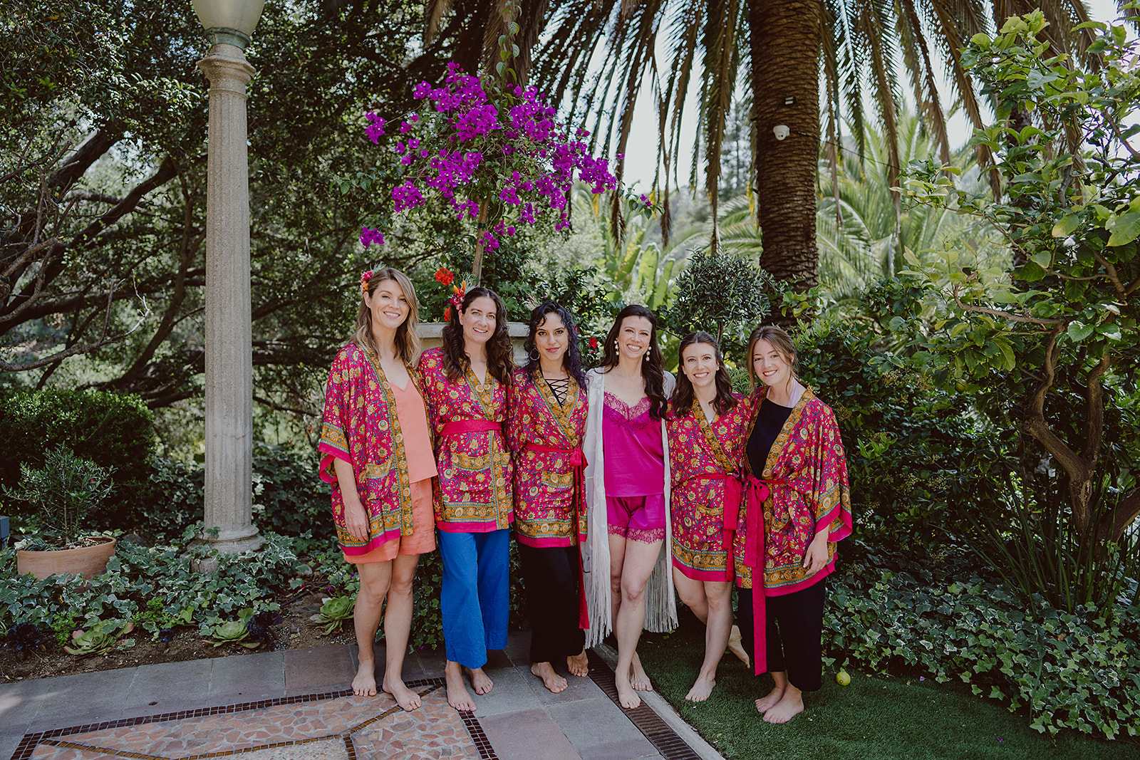 bride in fuchsia pajama set stands with bridesmaids in brightly colored robes