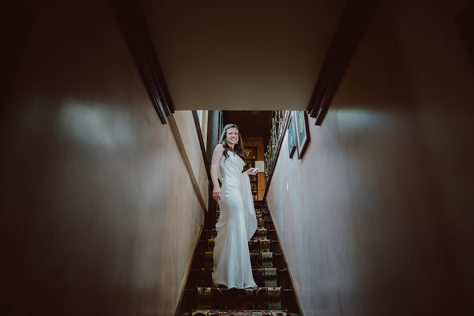 bride in minimalist satin wedding dress stands on staircase