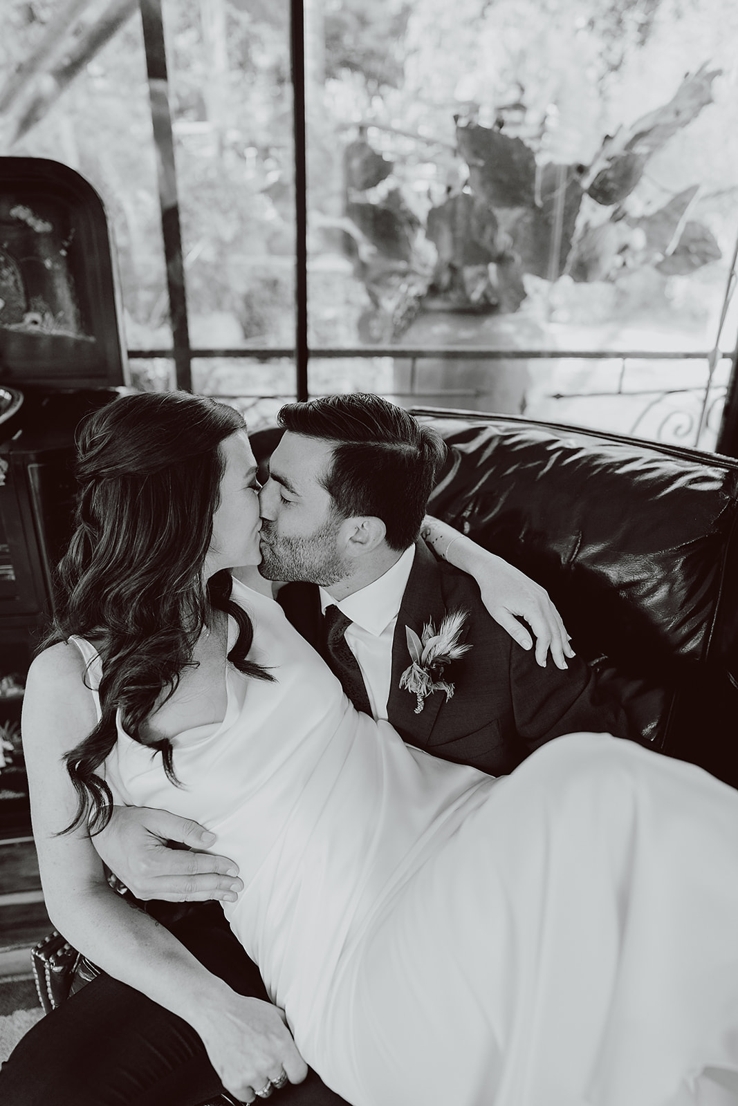 bride in minimalist satin wedding dress kisses groom in burgundy suit in a leather chair before their magical wedding at The Houdini Estate in Hollywood