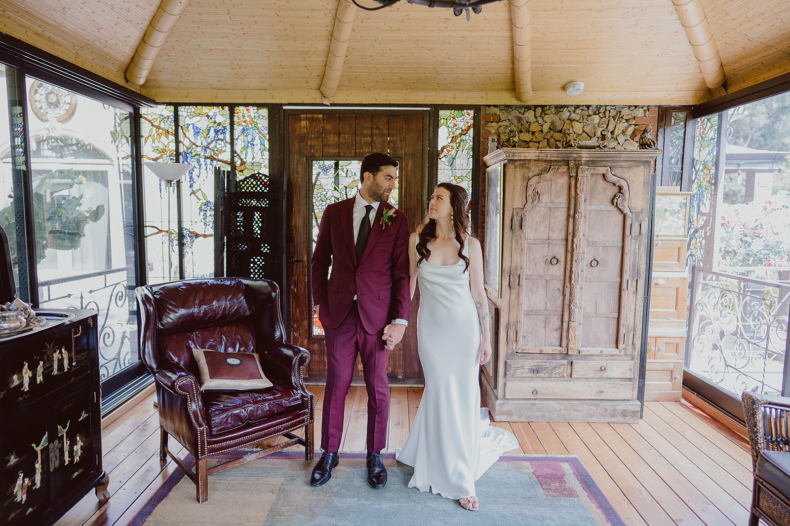 bride in minimalist satin wedding dress stands with groom in burgundy suit and black tie before their magical wedding at The Houdini Estate in Hollywood