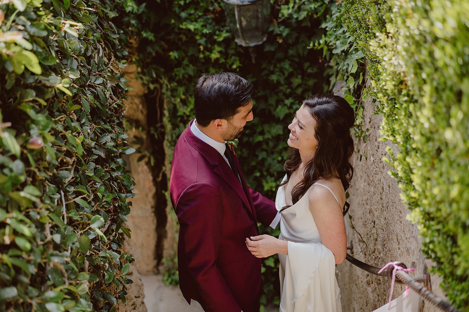 bride in minimalist satin wedding dress stands with groom in burgundy suit and black tie before their magical wedding at The Houdini Estate in Hollywood