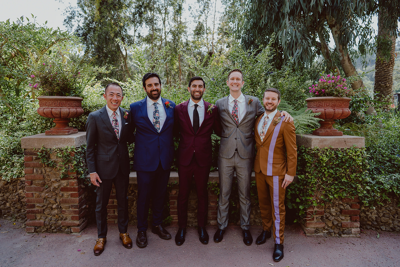 groom in Burgundy suit stands with groomsmen in mixed suits