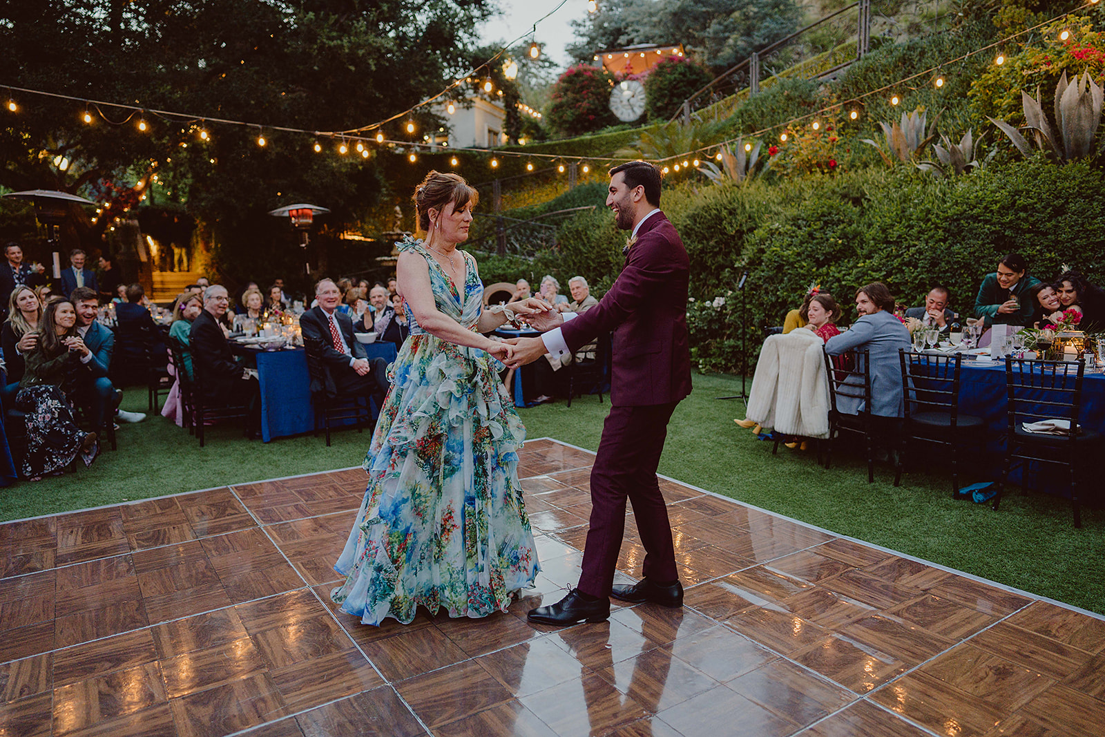 groom in burgundy suit dances with mother in watercolor dress