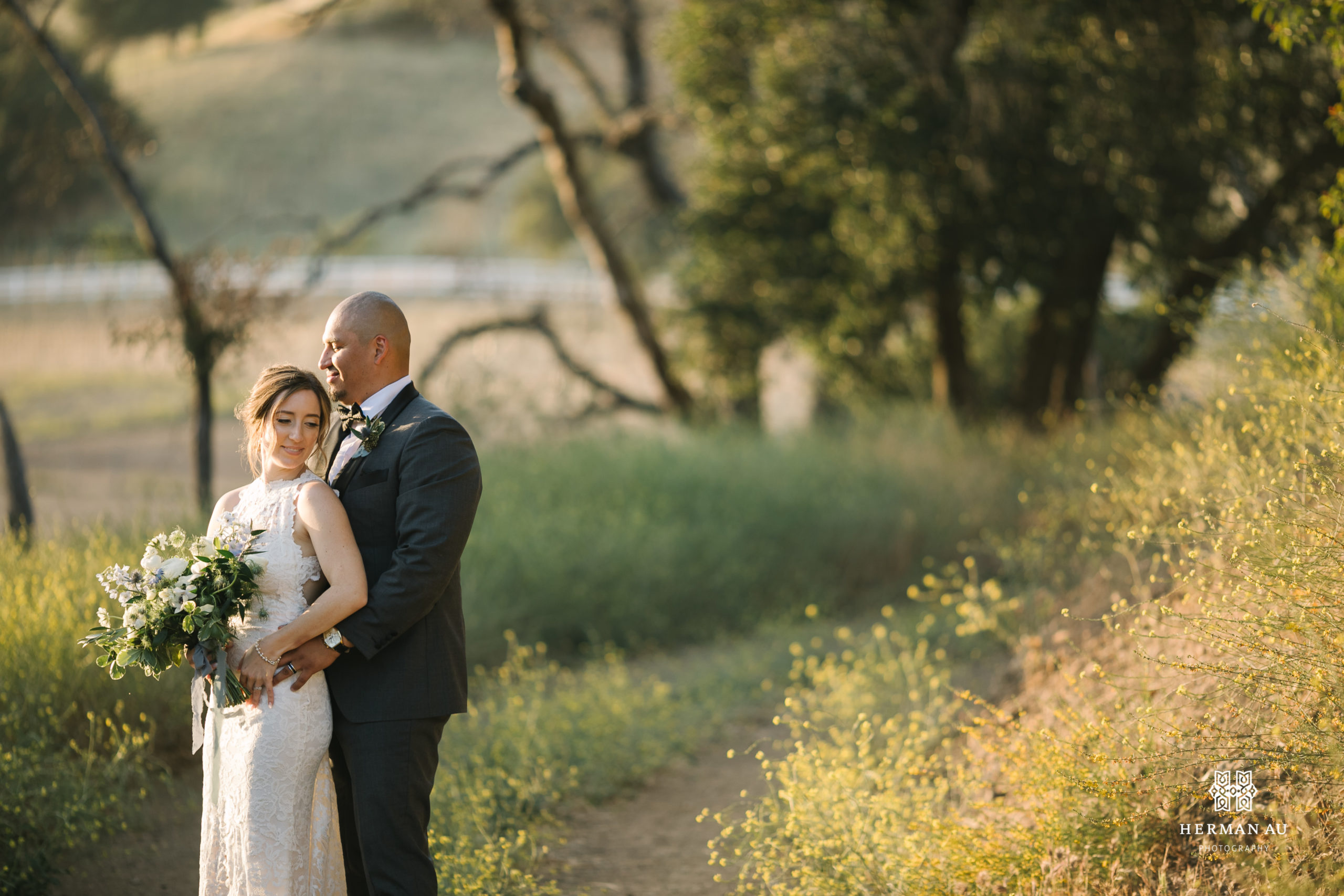 bride in high neckline open back lace wedding dress and groom in dark grey suit and black bowtie take photos in vineyard at Saddlerock Ranch