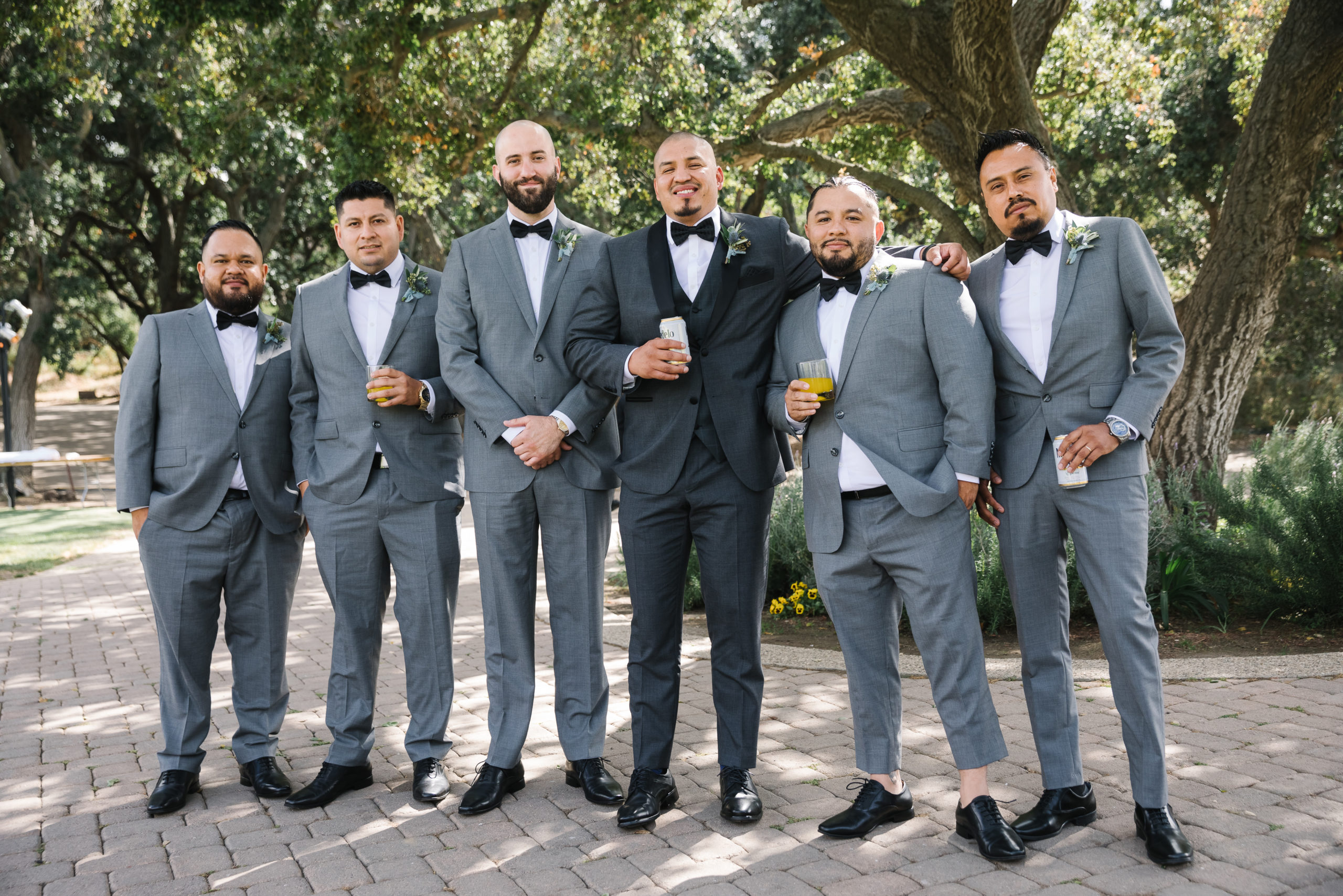 groom in dark grey suit and black bowtie stands with groomsmen in light grey suits and black bowties 