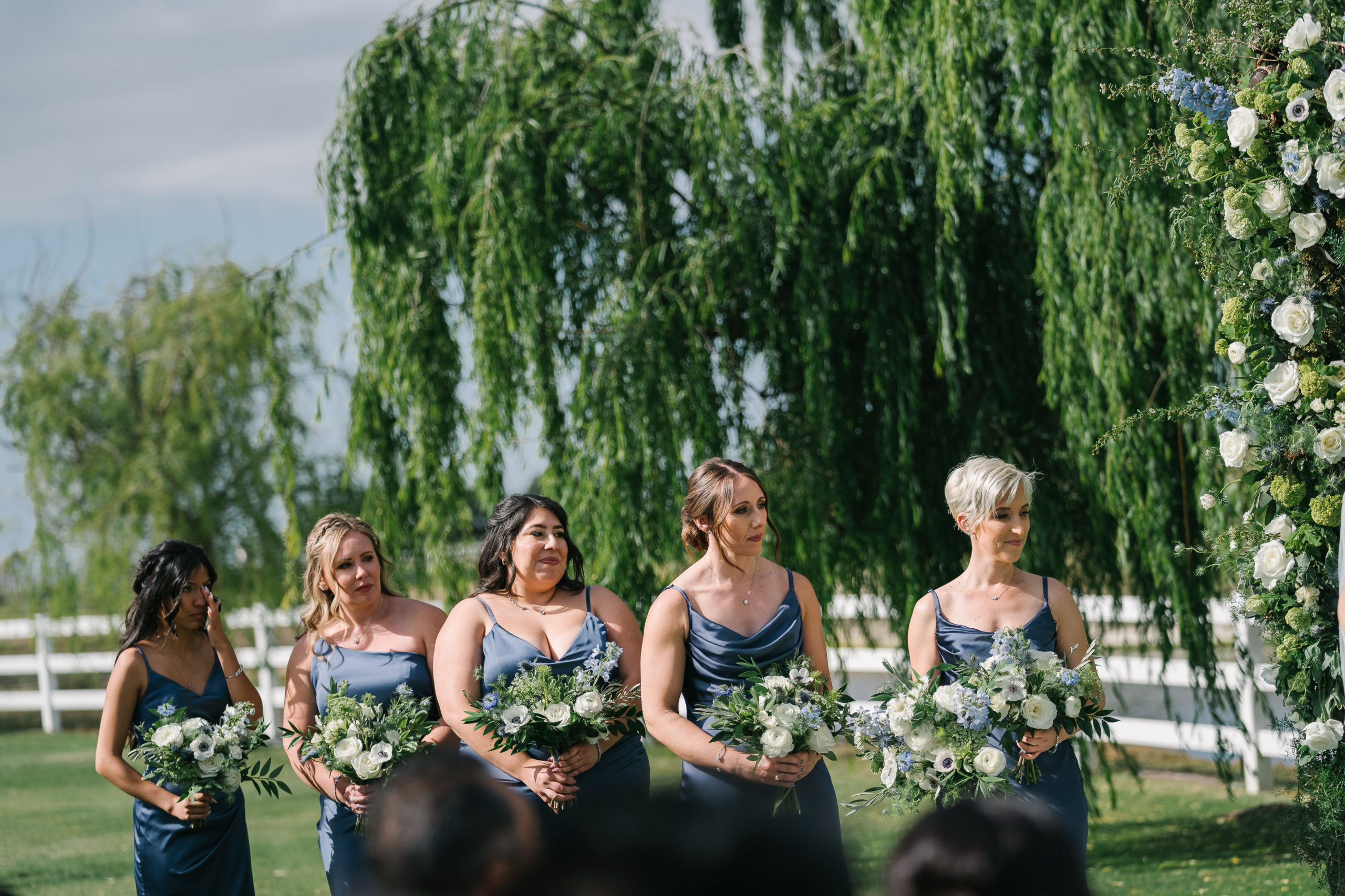 emotional bridesmaids in dark blue satin dresses stand during wedding ceremony at Saddlerock Ranch