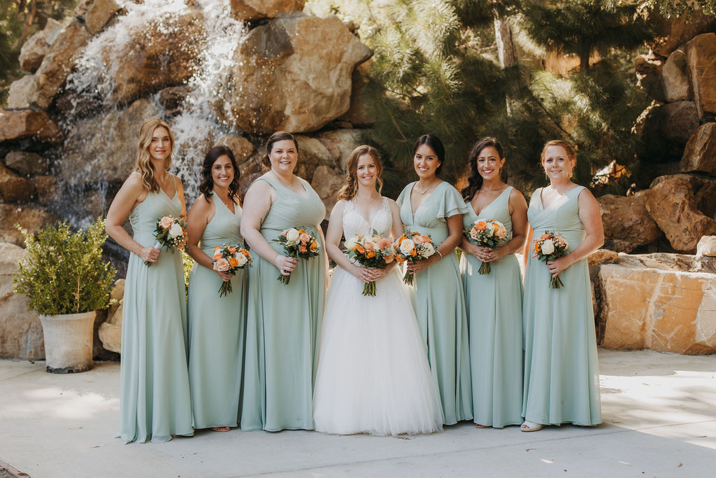 bride in v-neck tulle ball gown stands with bridesmaids in mint green dresses in front of waterfall at Calamigos Ranch