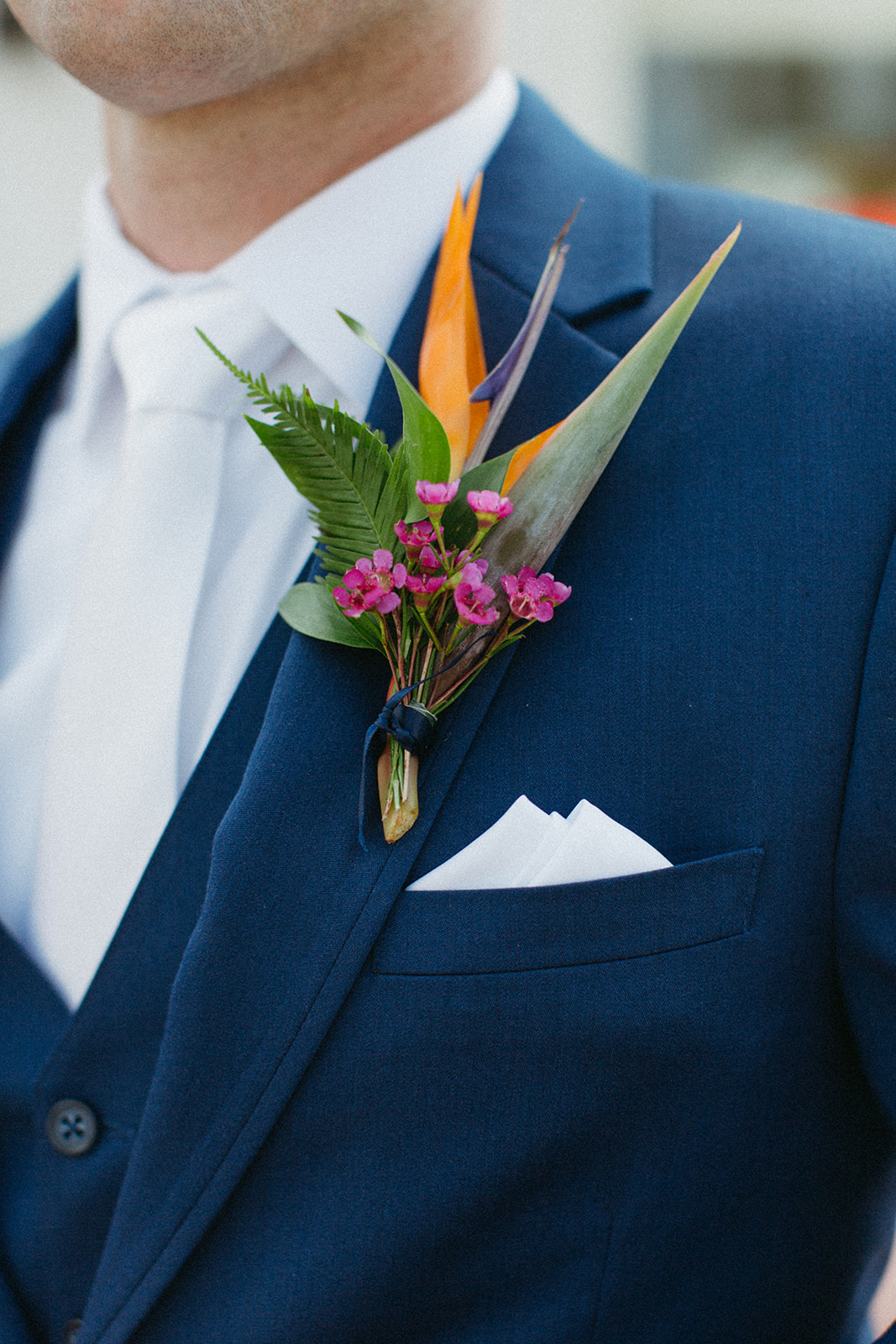 groom in blue suit and white tie with brown shoes and a colorful tropical boutonniere 