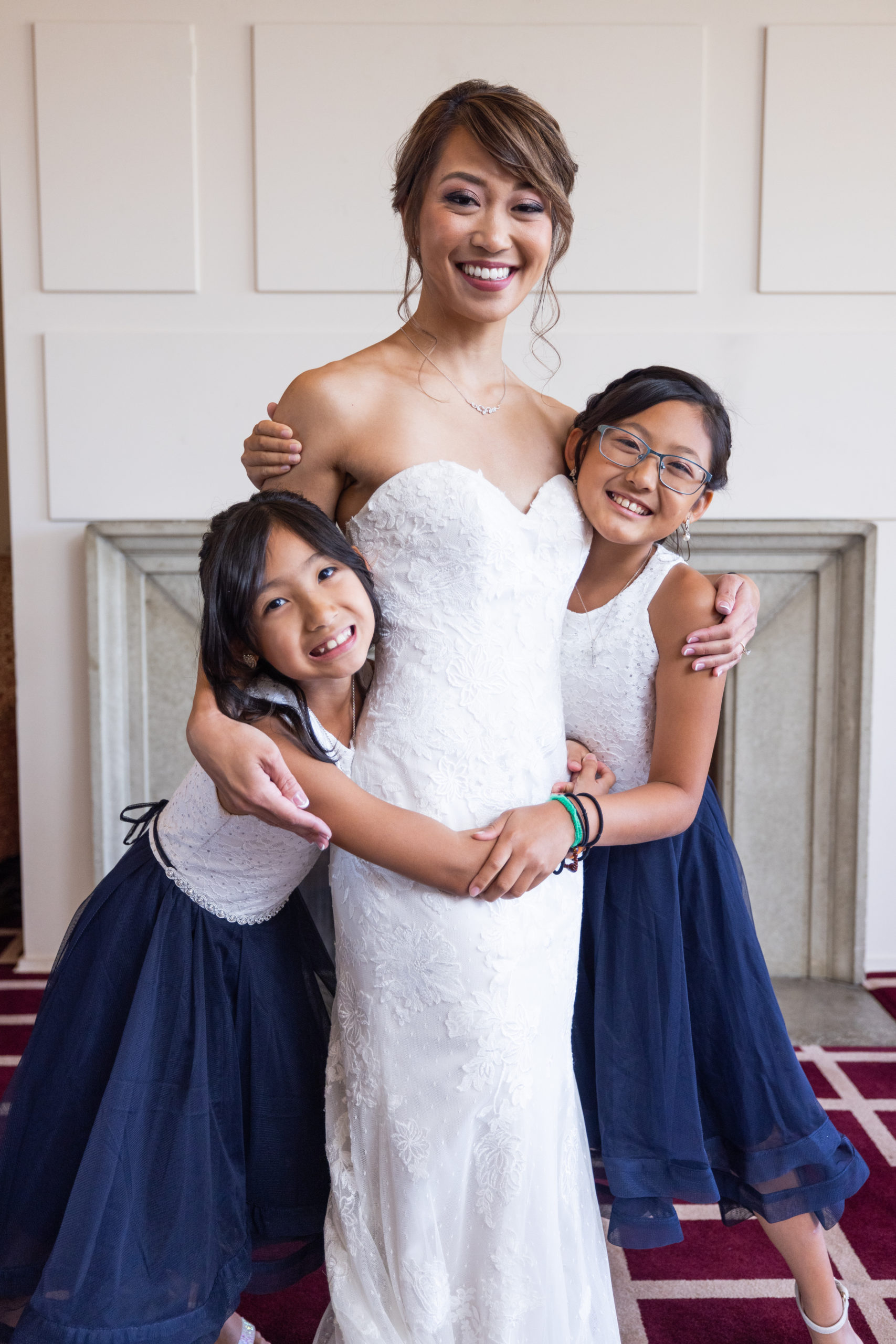 bride in strapless lace wedding dress wearing low chignon bun with flower girls in navy blue skirts