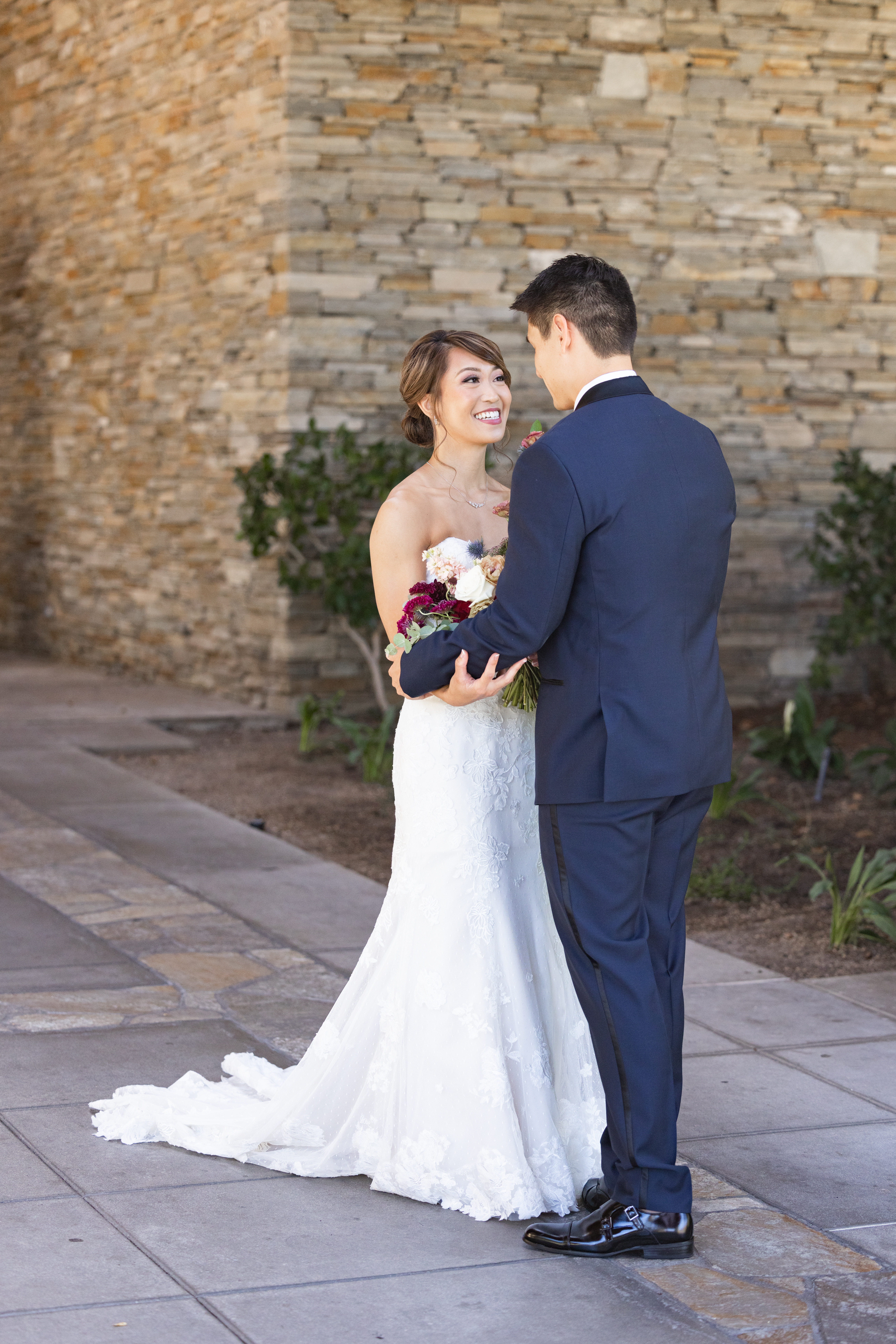 first look with bride in strapless wedding dress and jewel toned bridal bouquet and groom in navy tuxedo suit with black lapels, grey vest and maroon tie