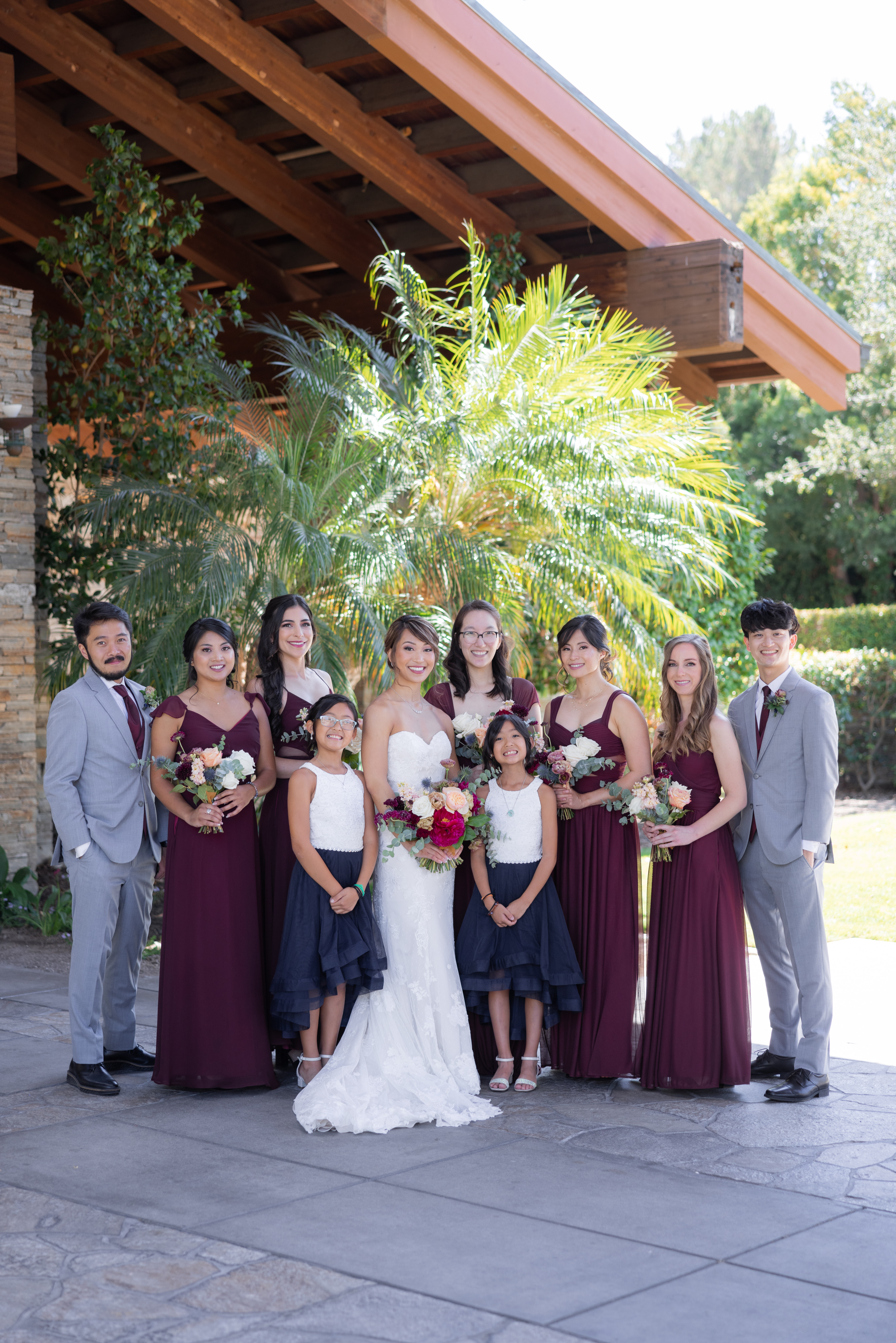 bride in strapless wedding dress and jewel toned bridal bouquet stand with co-ed wedding party wearing maroon 