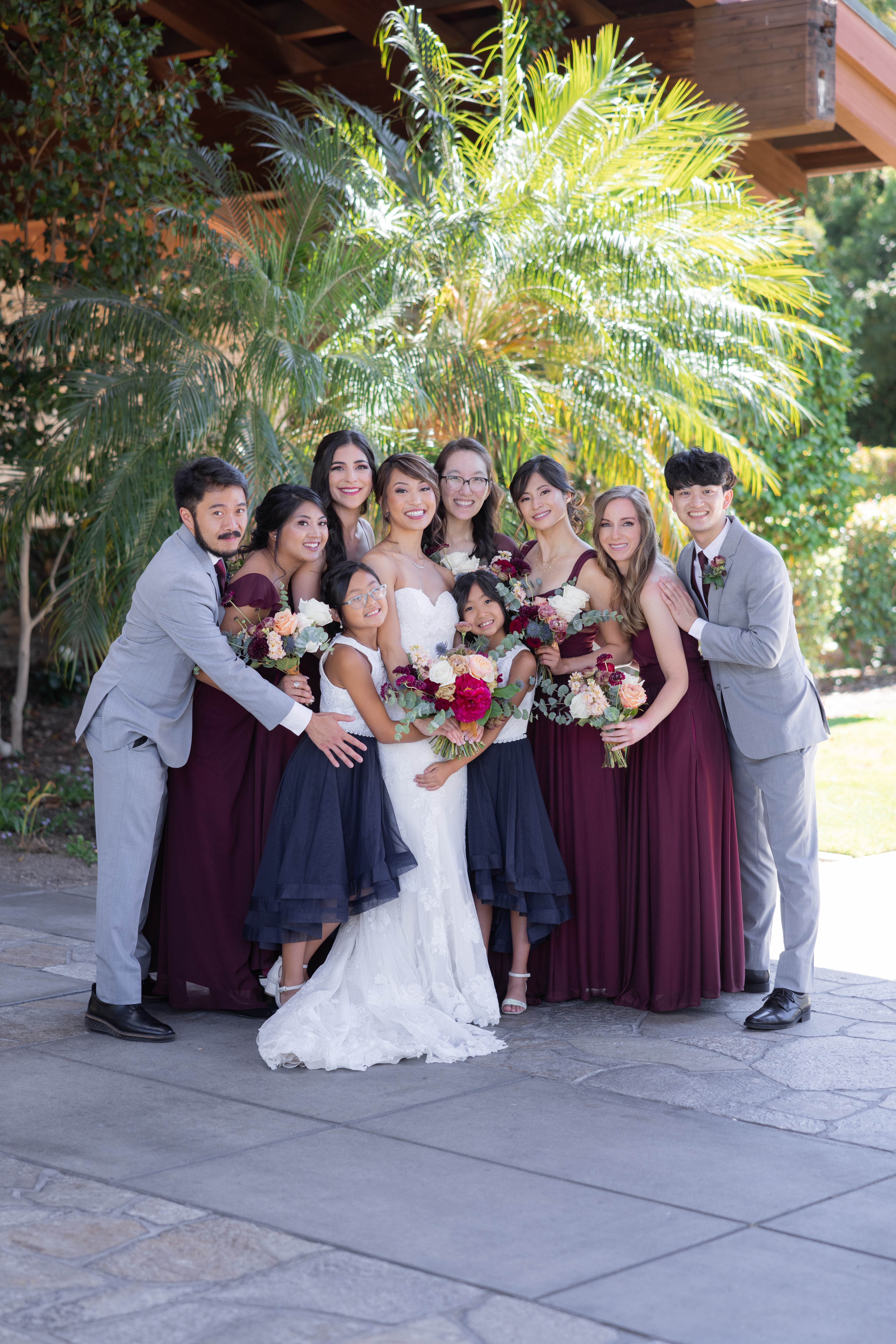 bride in strapless wedding dress and jewel toned bridal bouquet  stand with co-ed wedding party in maroon