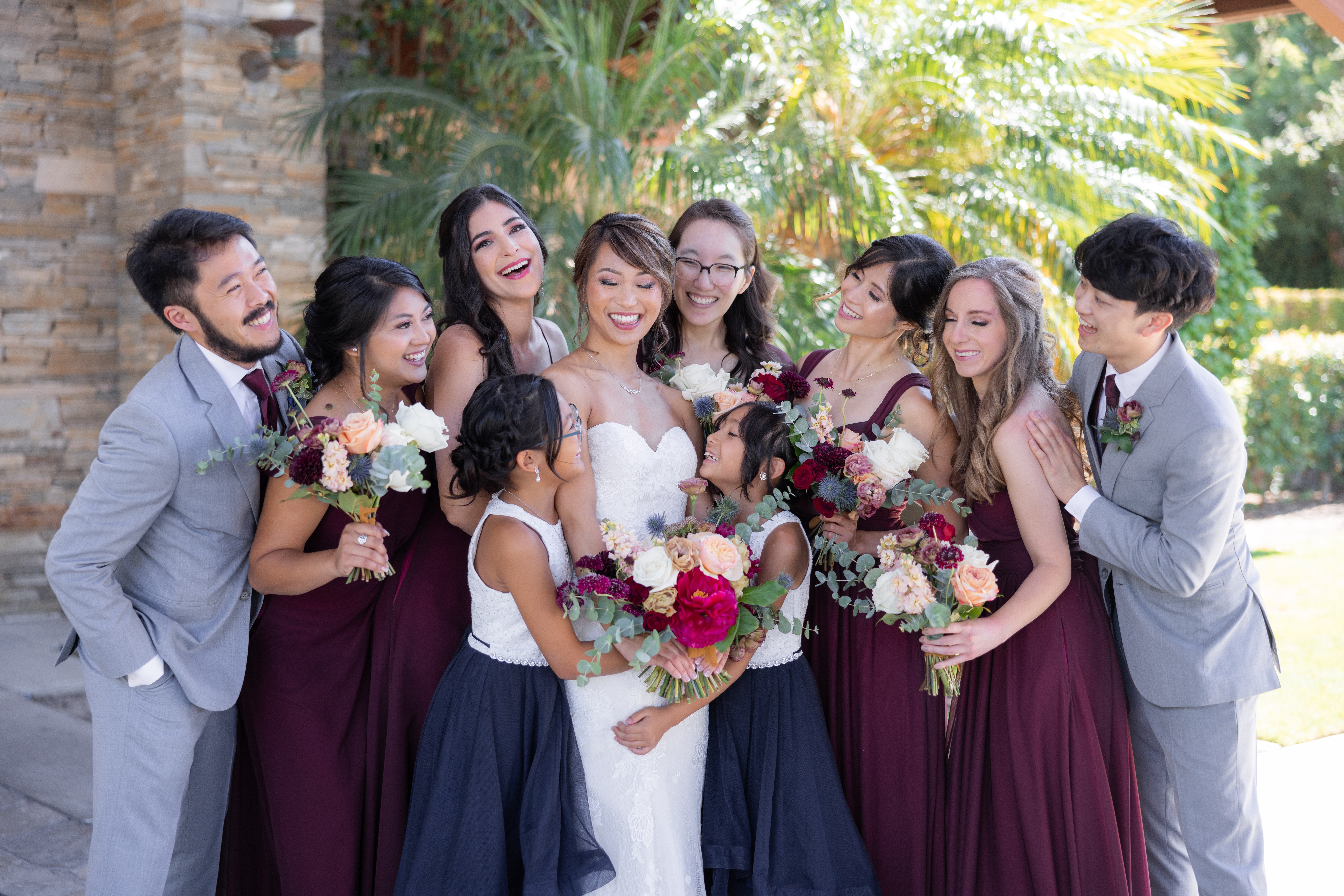 bride in strapless wedding dress and jewel toned bridal bouquet stand with co-ed wedding party in maroon
