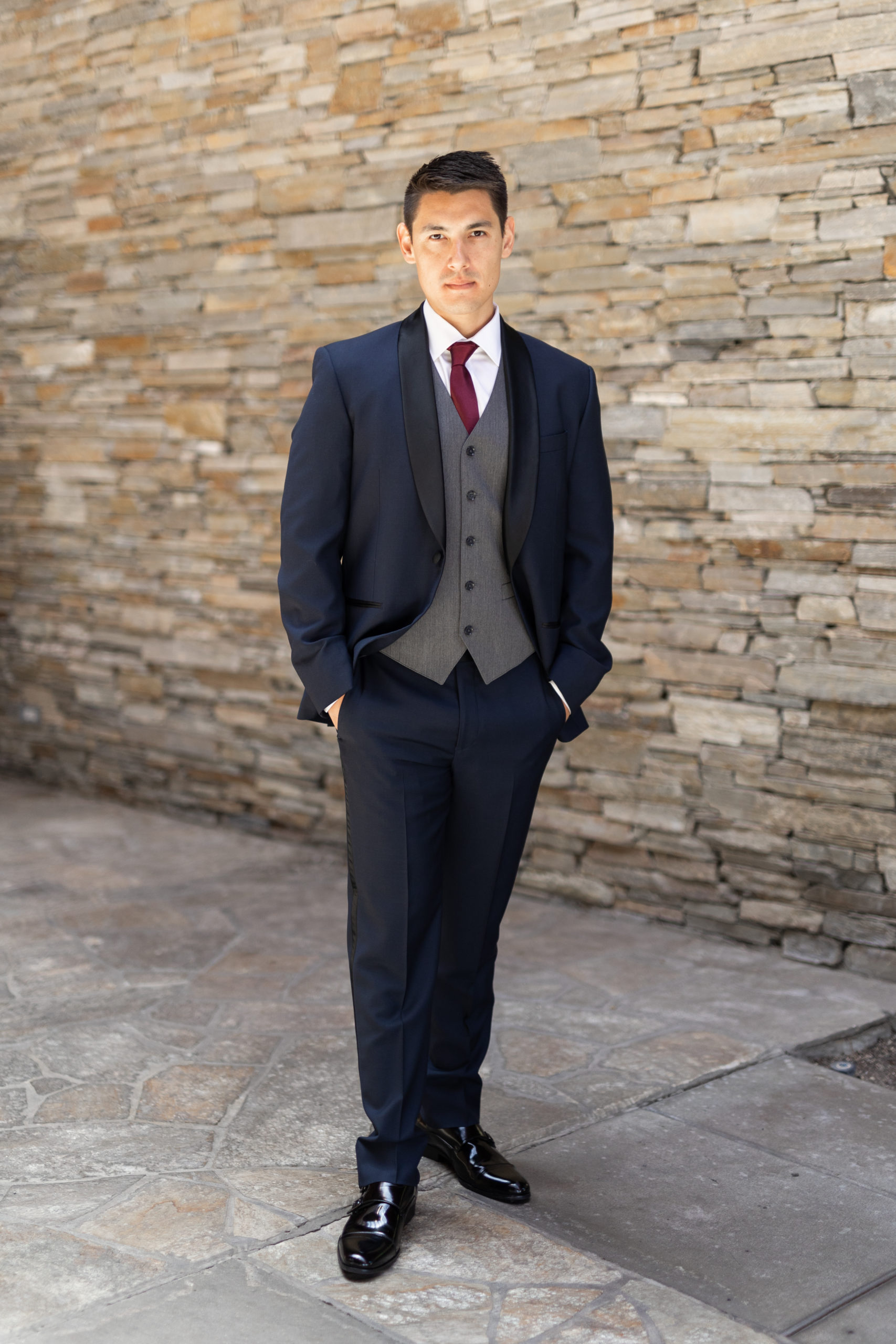 groom in navy tuxedo suit with black lapels, grey vest and maroon tie 