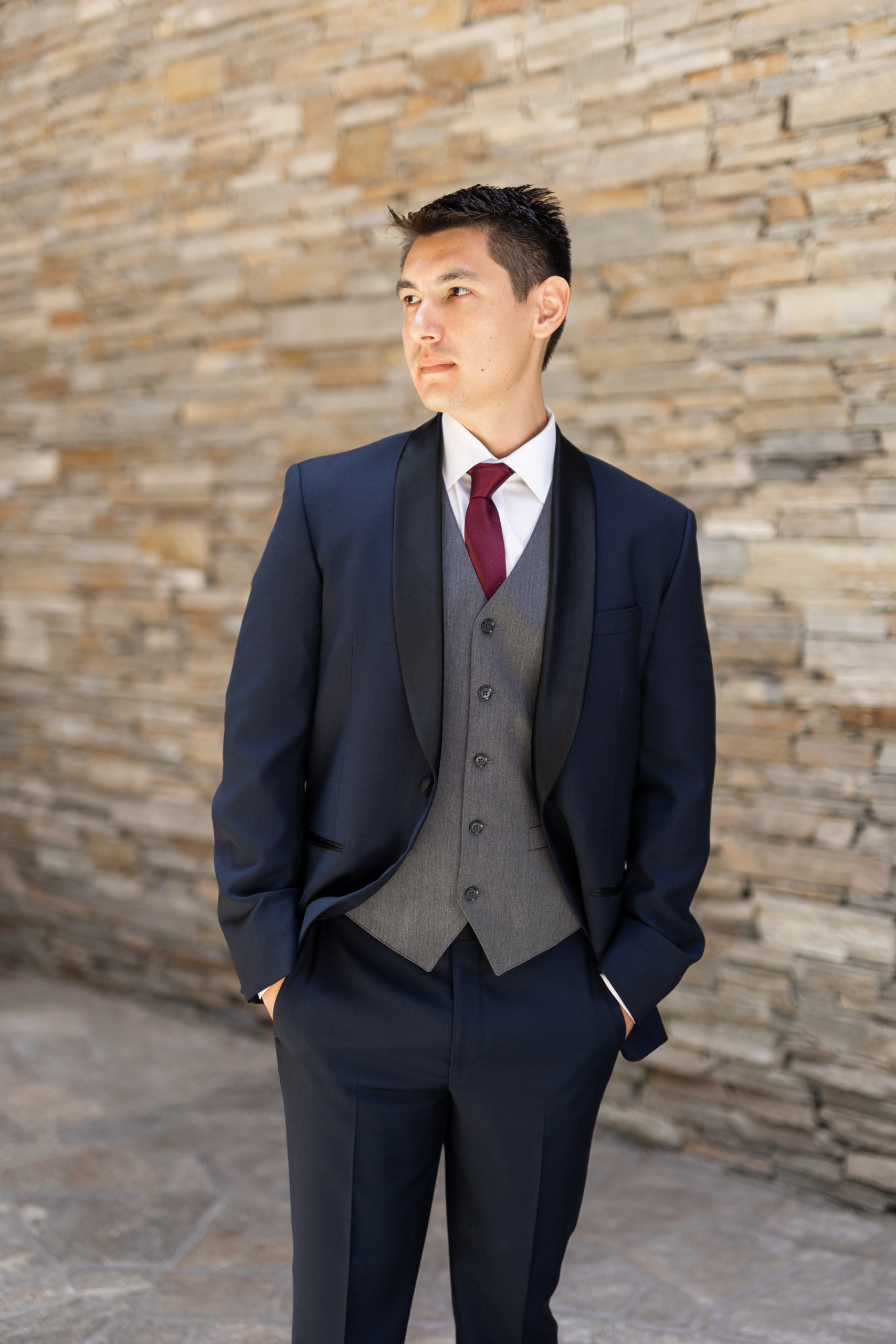 groom in navy tuxedo suit with black lapels, grey vest and maroon tie 