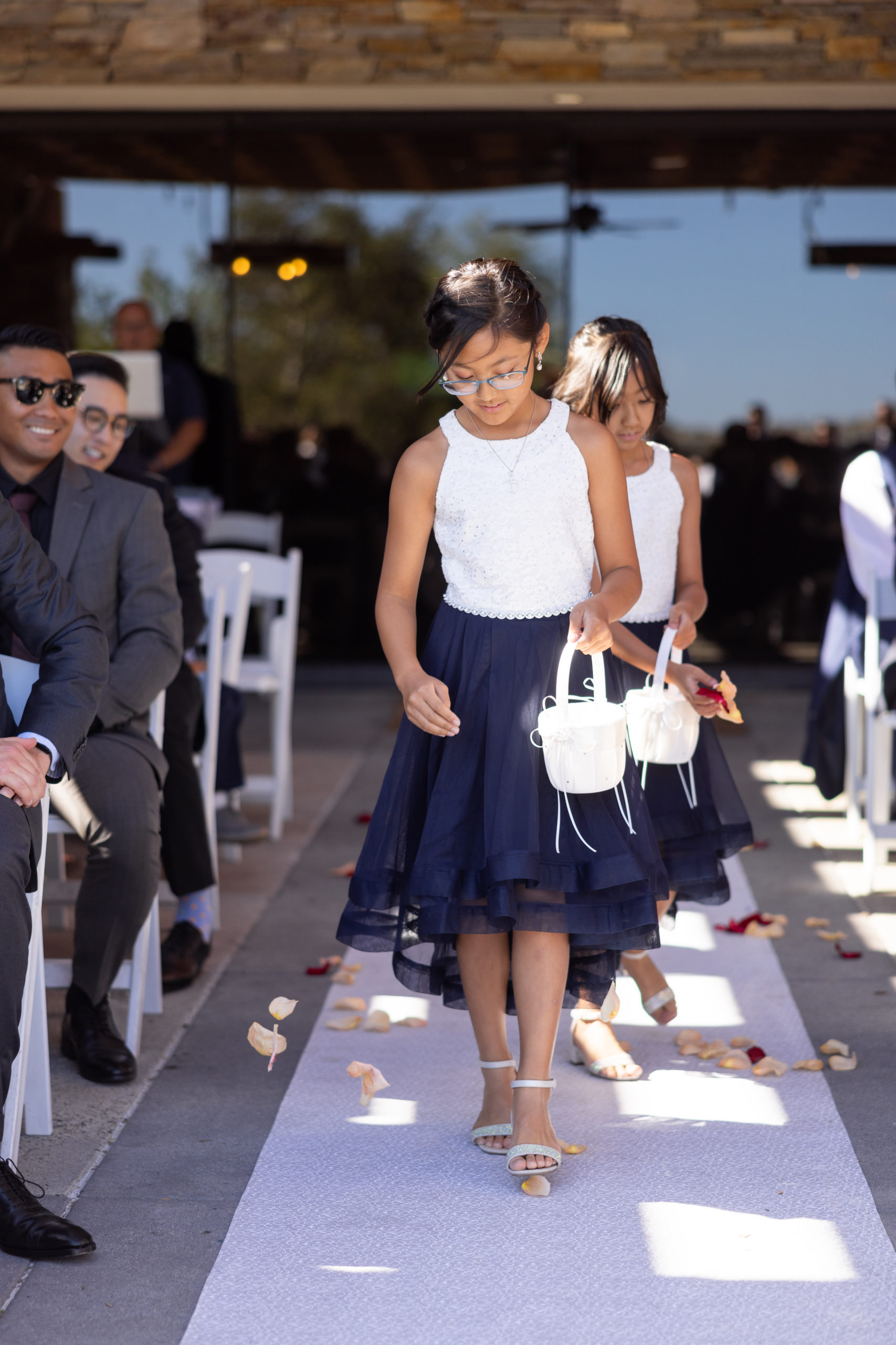 flower girls in white and navy dresses walking down the aisle 