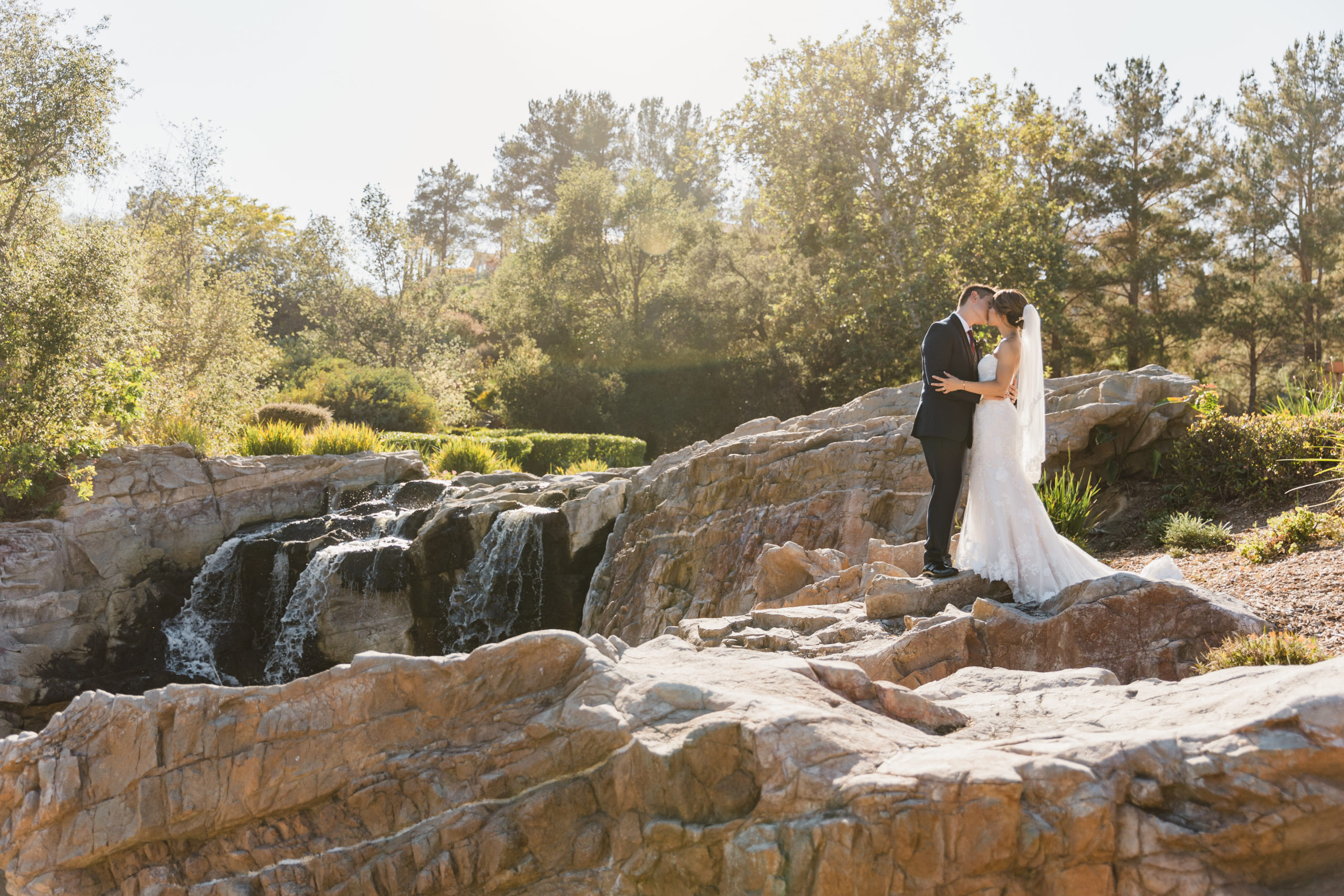 bride in strapless lace wedding dress and groom in navy tuxedo take outdoor portrait photos by waterfall at Dove Canyon Golf Club
