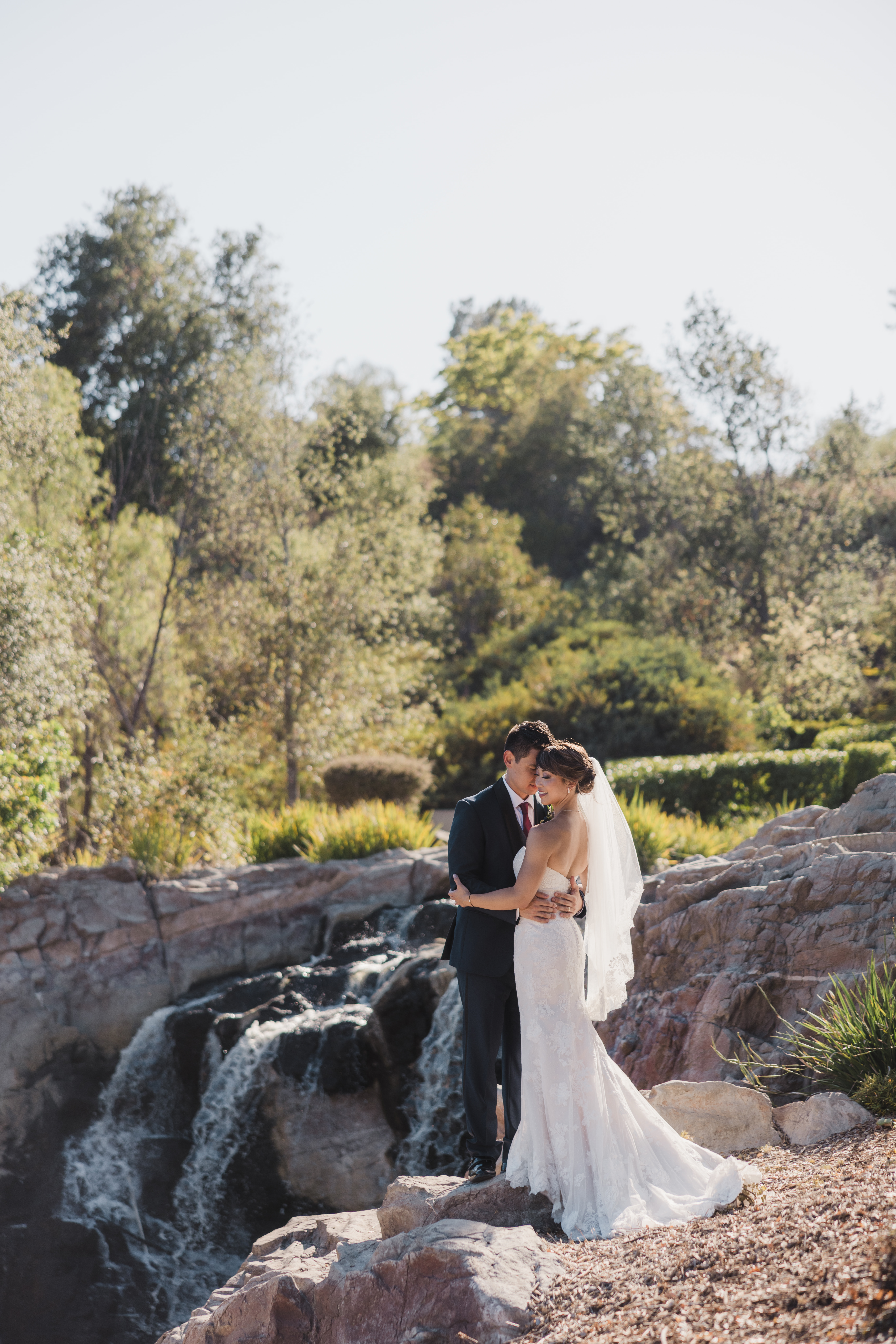 bride in strapless lace wedding dress and groom in navy tuxedo take outdoor portrait photos by waterfall at Dove Canyon Golf Club