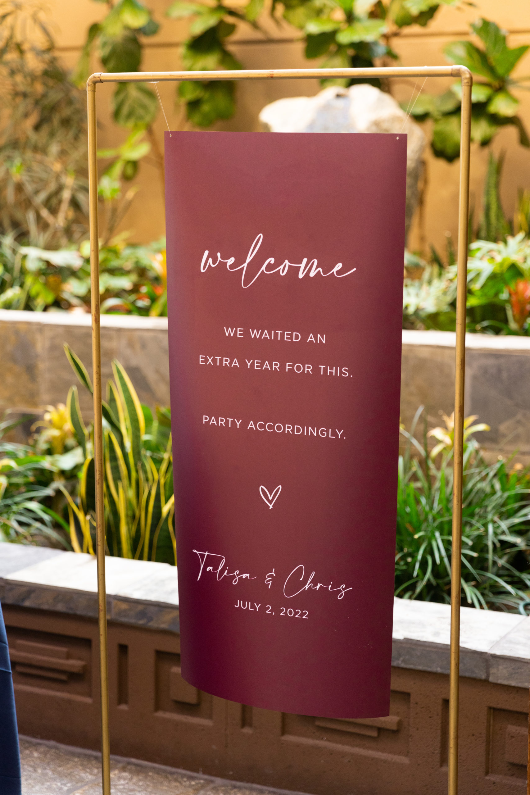 maroon postponed wedding welcome sign that reads "We waiting an extra year for this. Party accordingly"