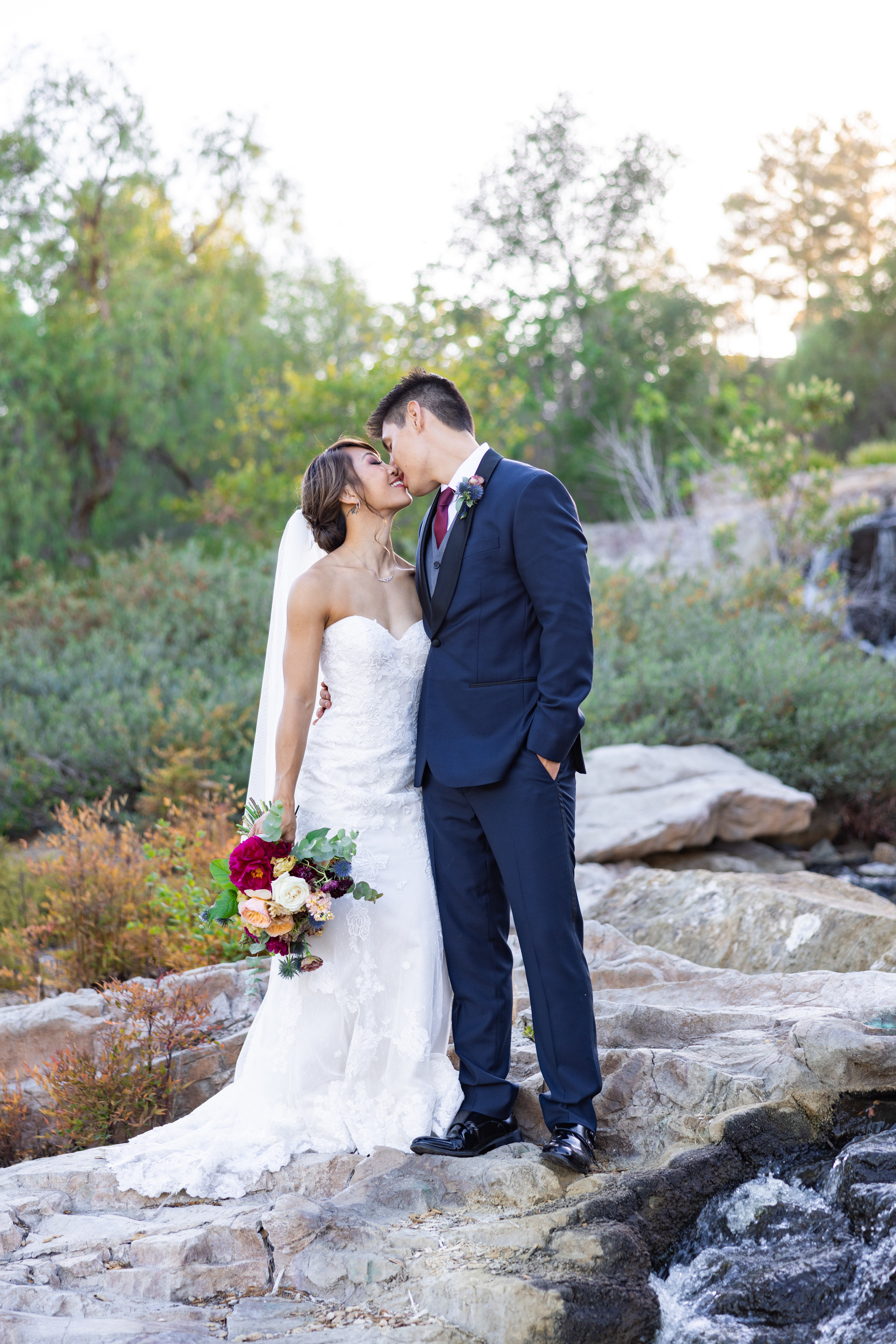 bride in strapless lace wedding dress and groom in navy tuxedo take outdoor sunset portrait photos by waterfall at Dove Canyon Golf Club