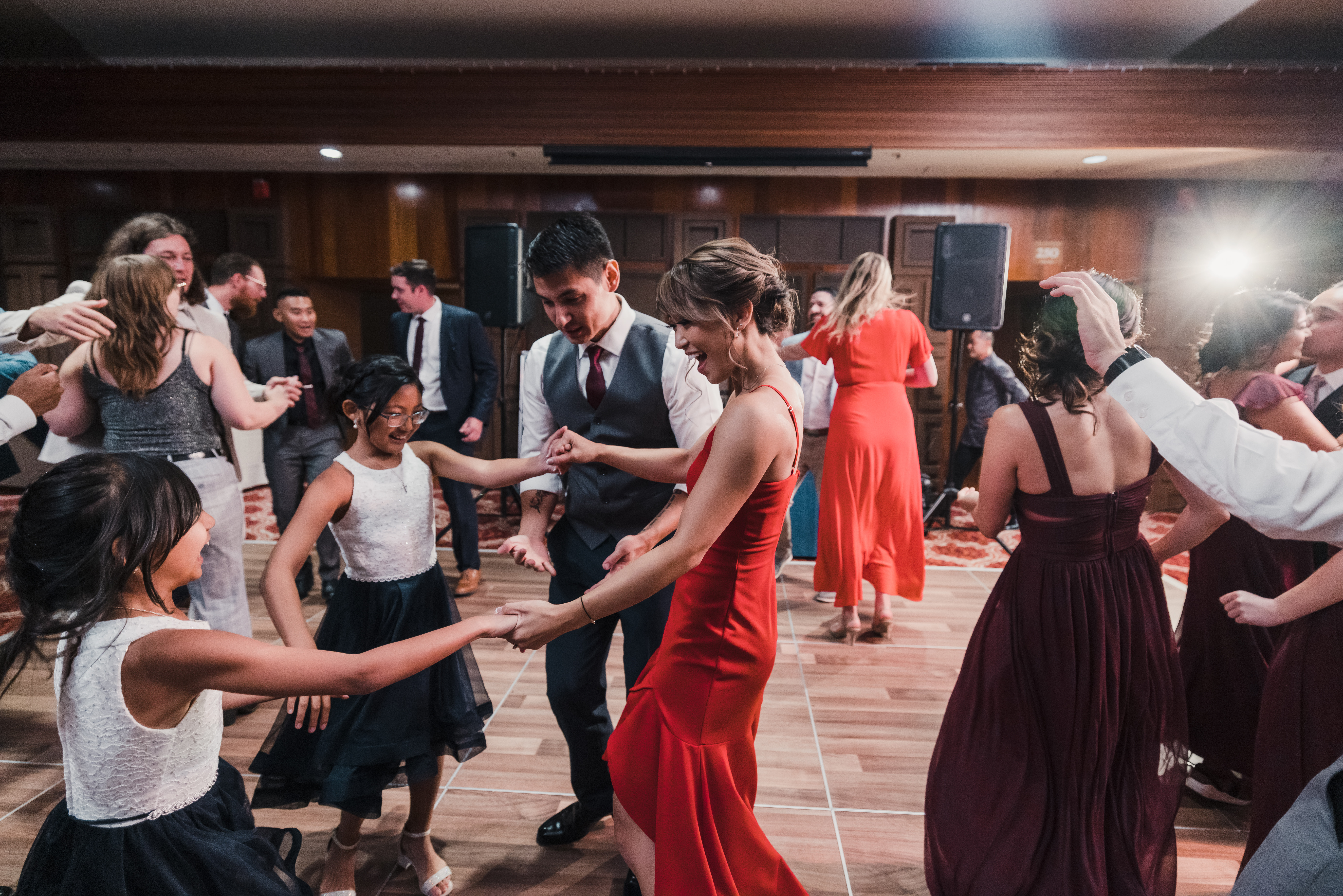 bride in red reception dress and groom dance with guests