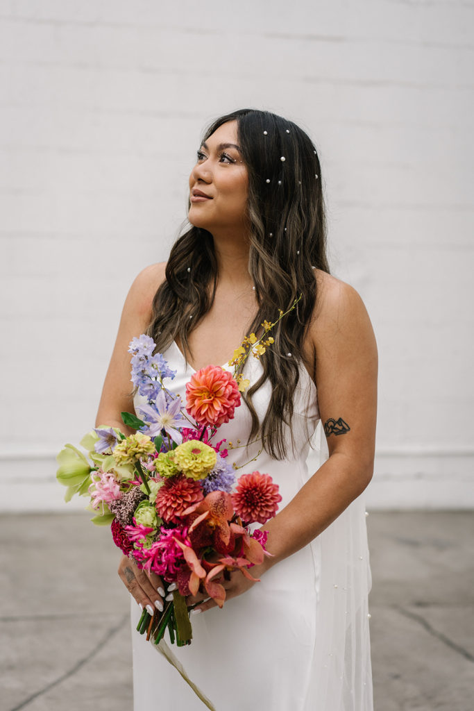 bride in modern silk wedding dress with pearls in hair holding bright colorful bridal bouquet
