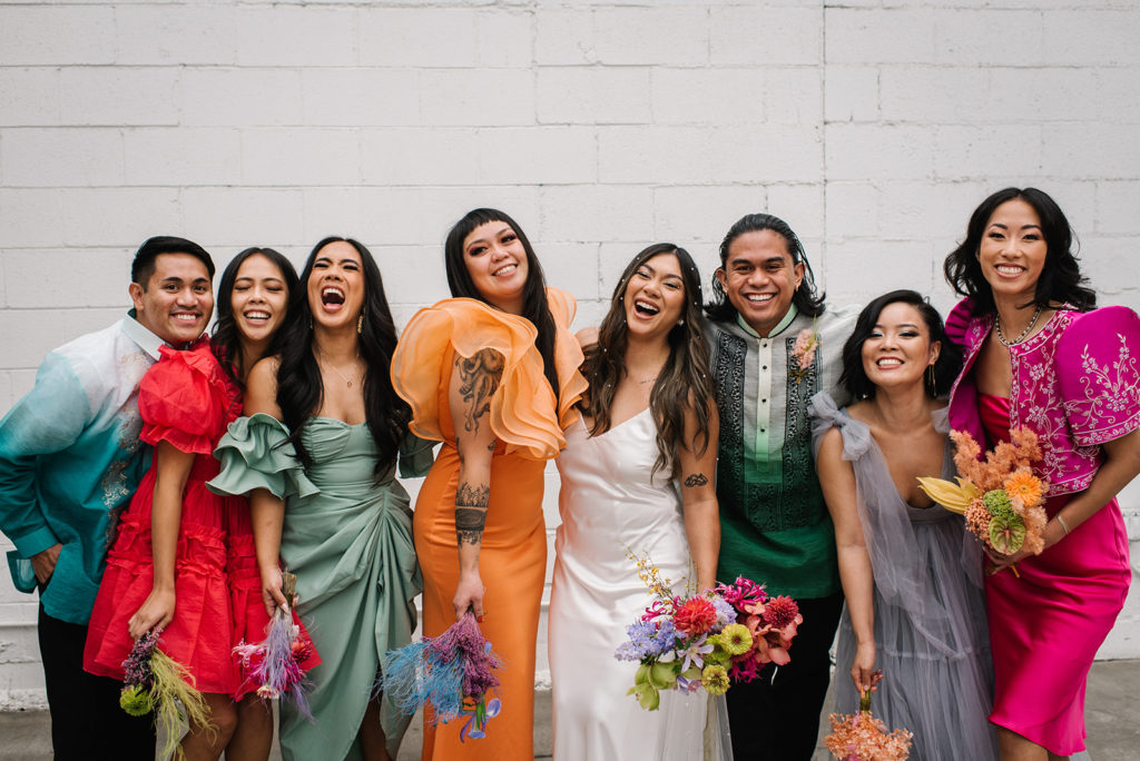 bride in modern silk wedding dress stands with co-ed wedding party in colorful rainbow inspired outfits