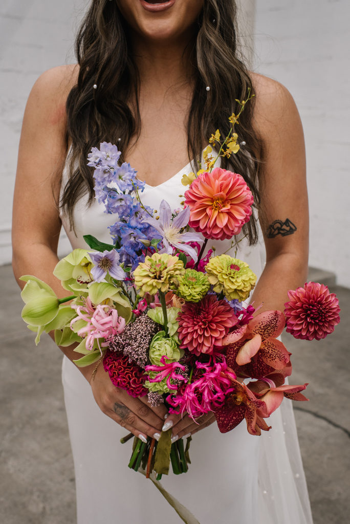bride in modern silk wedding dress with pearls in hair holding bright colorful bridal bouquet