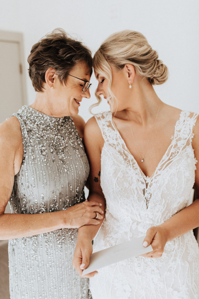 bride in neck Champagne dress with beaded lace overlay stands with with mother in silver beaded dress