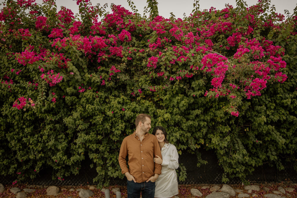 mid-century inspired desert engagement photo session with bride to be in silk mini dress and groom in brown button up in front of bougainvillea