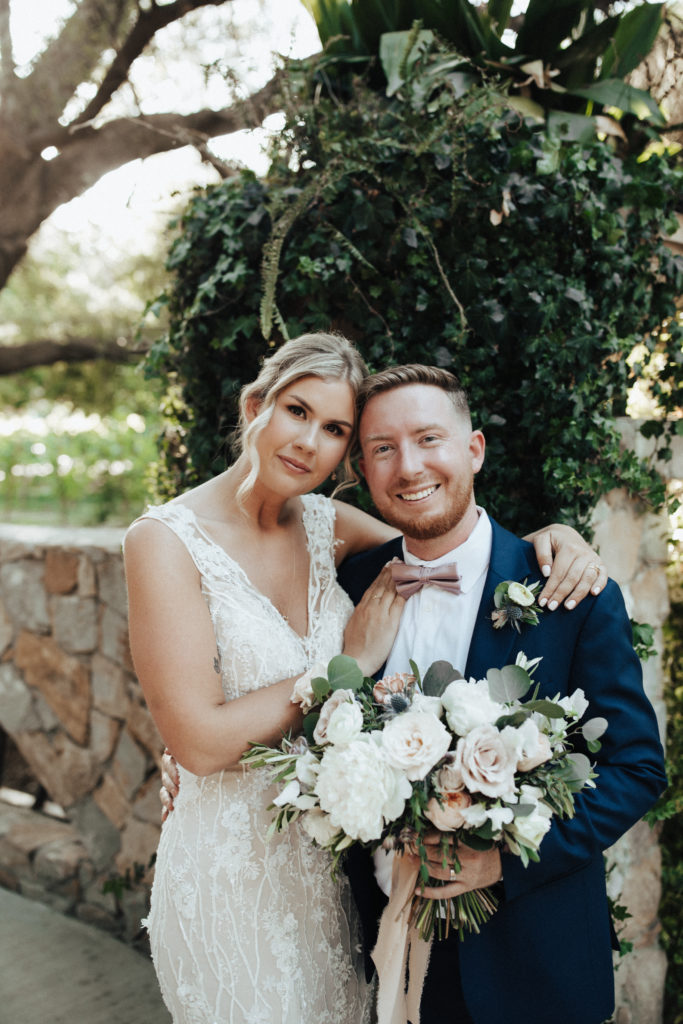 bride in deep v-neck wedding dress with soft pink and white bridal bouquet stands with groom in navy suit and pink bowtie
