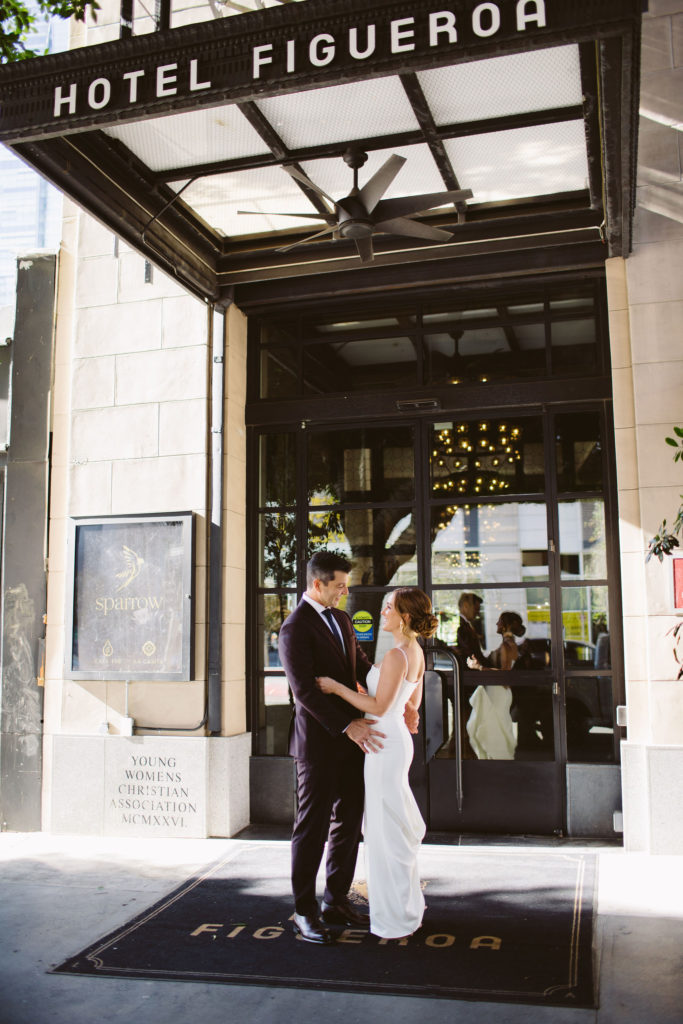 bride in modern square neck spaghetti strap wedding dress and groom in deep plum suit take portrait shots at Hotel Figueroa