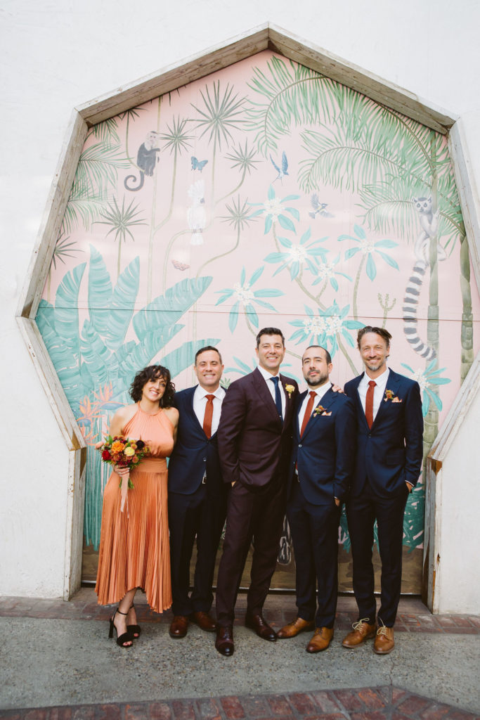 groom in plum suit with co-ed wedding party in blue suits and orange dress 