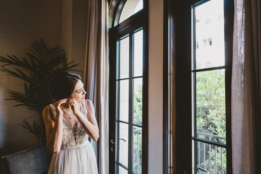 bride puts on earrings while looking out the window