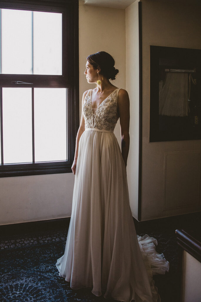 bride in embellished deep v neck wedding dress with a chiffon skirt stands in hotel hallway
