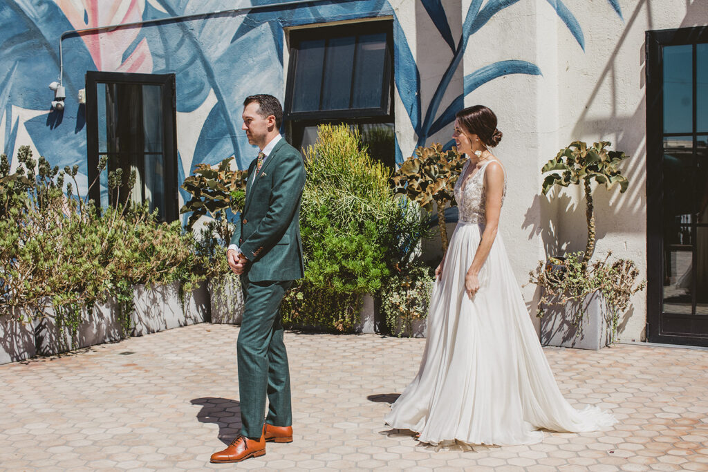 bride in embellished deep v neck wedding dress with a chiffon skirt does first look with groom in custom green suit at Hotel Figueroa