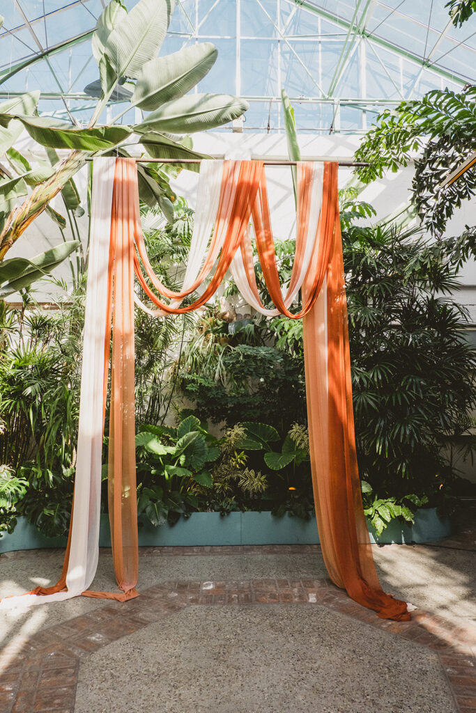 ceremony area with peach and orange chiffon draping arch surrounded by greenery at Valentine DTLA
