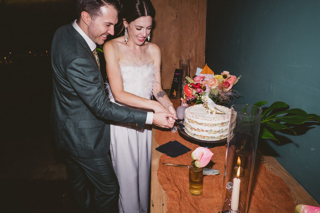 bride and groom cutting wedding cake with gold dinosaur toppers