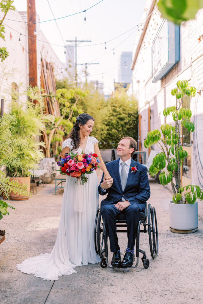 bride holding brightly colored bouquet with groom in navy blue suit and silver tie before their fiesta themed wedding at The Grass Room