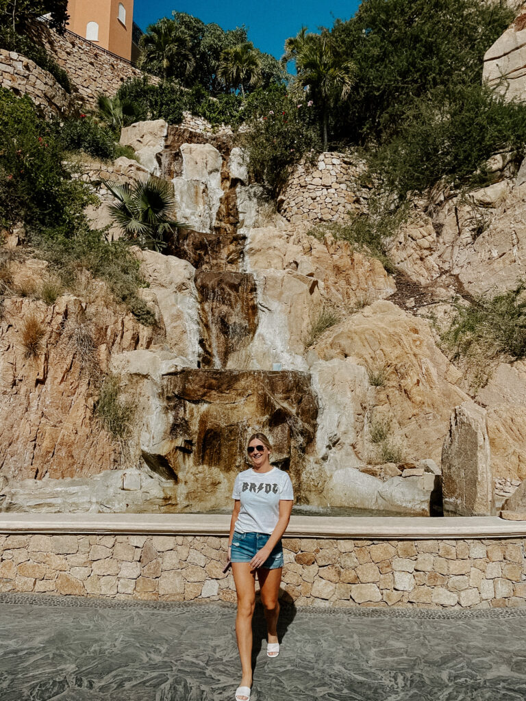 Kari of Feathered Arrow Events in white t-shirt with rocker Bride print in front of waterfall in Cabo