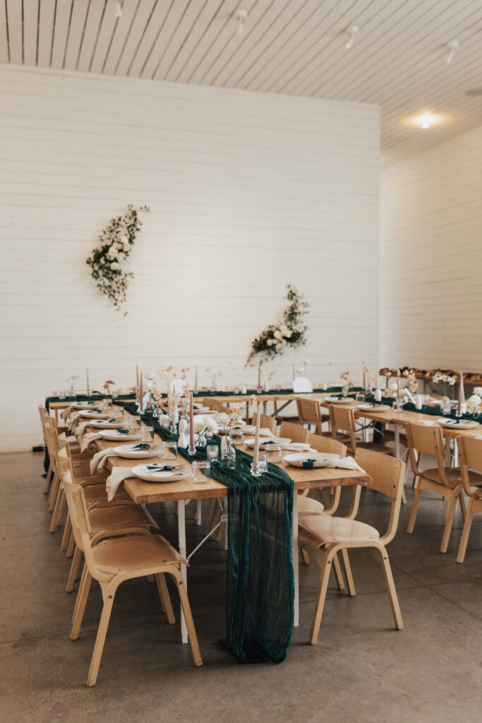 Modern wedding reception at Prospect House with wooden oak chairs and tables, dark green linens, beige taper candles and small bud vases