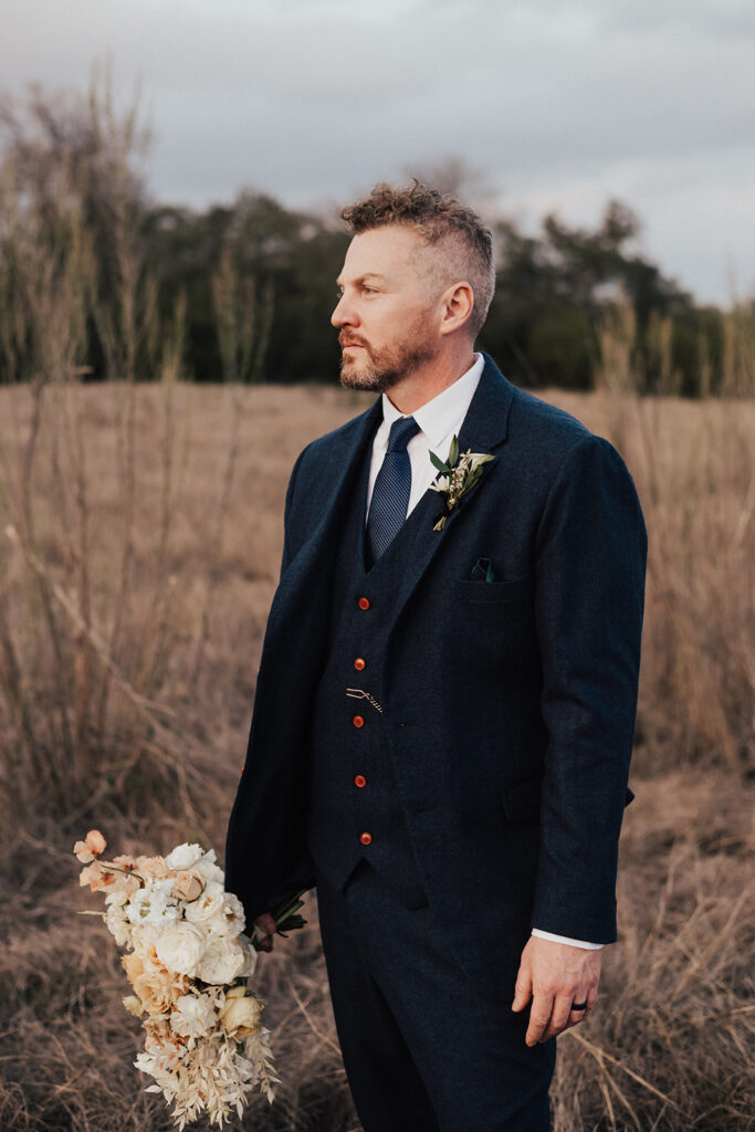 groom in navy blue suit holds bridal bouquet