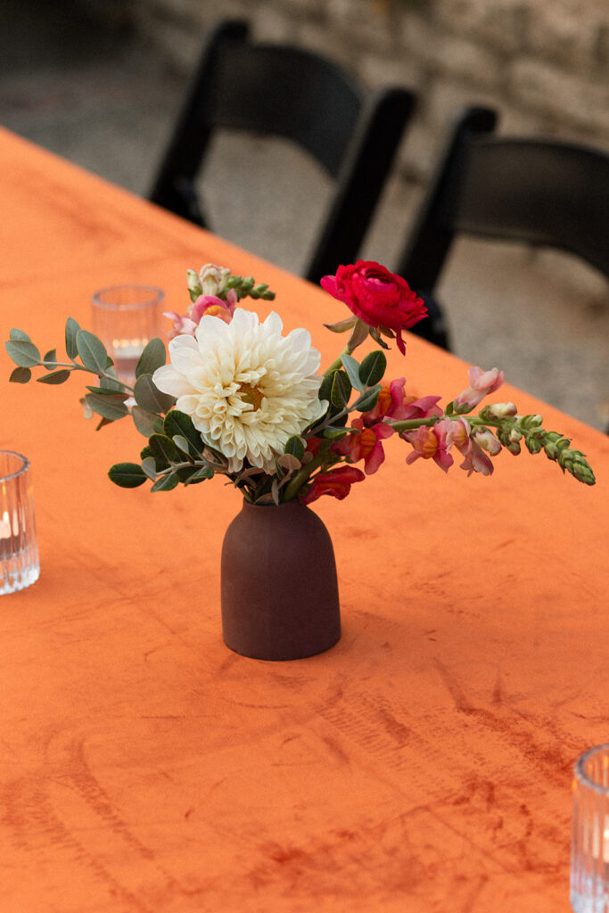 terracotta vase with flower arrangement on bright orange velvet table cloth