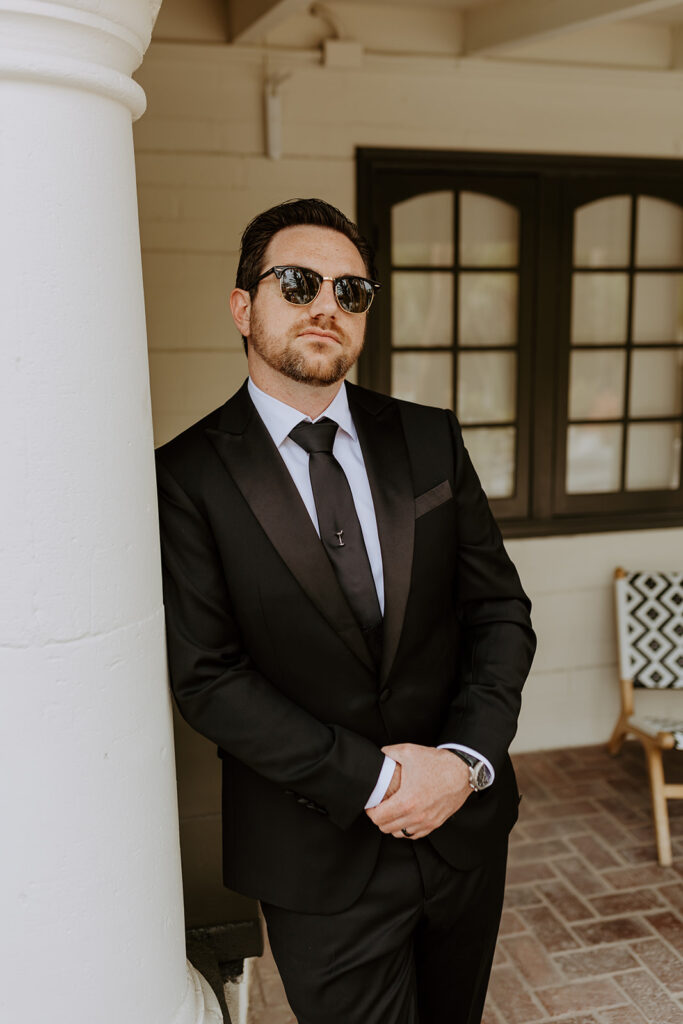 groom in black suit and sunglasses stands by pool side
