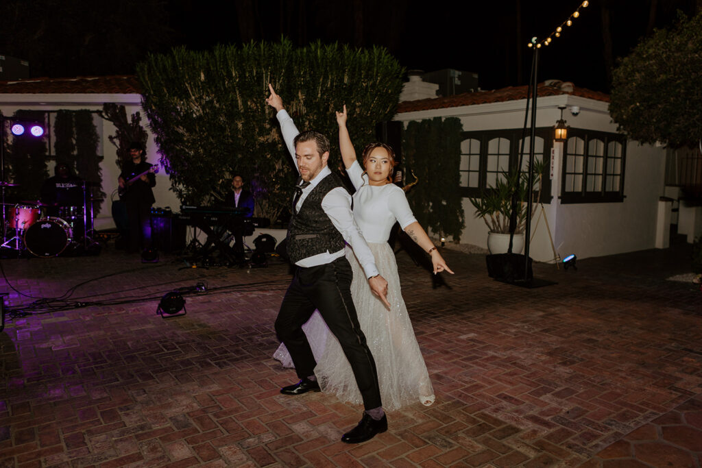 bride in two piece wedding reception shirt and skirt dances with groom in black suit during pool side wedding reception at Villa Royale Palm Springs