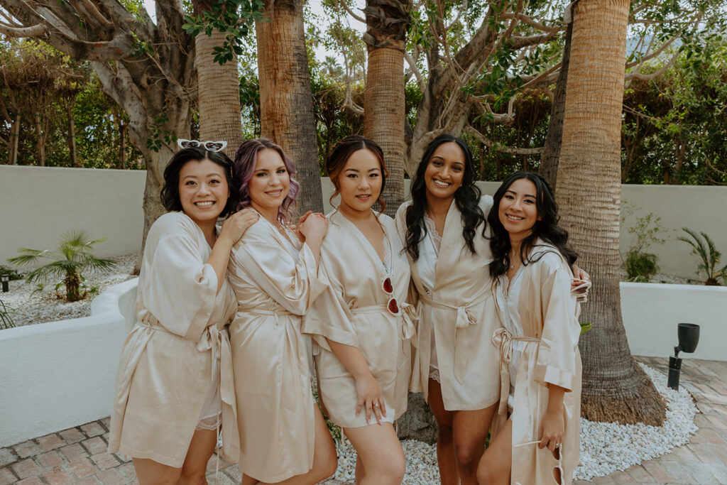 bride with bridesmaids in beige satin robes and heart shaped sunglasses