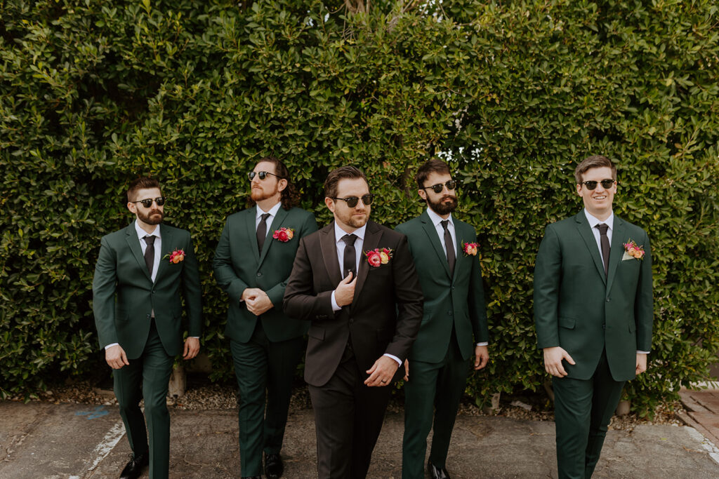 groom in black suit stands with groomsmen in dark green suits