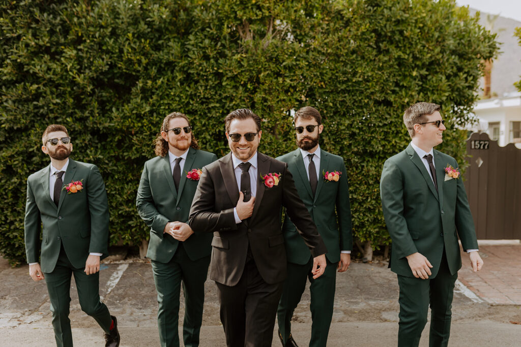 groom in black suit stands with groomsmen in dark green suits