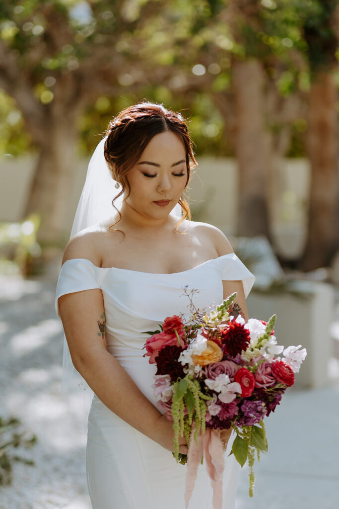 bride in minimalist off shoulder wedding dress with colorful bouquet and veil with pearls poses for portrait shots in Palm Springs