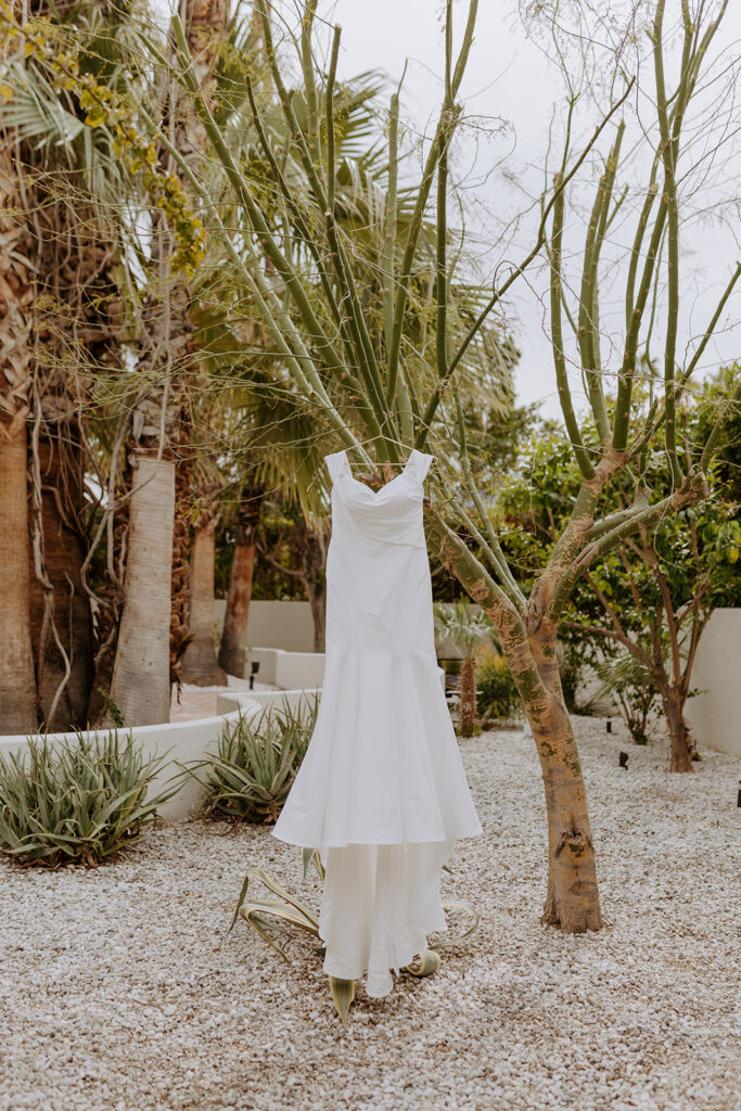 off shoulder minimalist wedding dress hanging from tree in desert courtyard